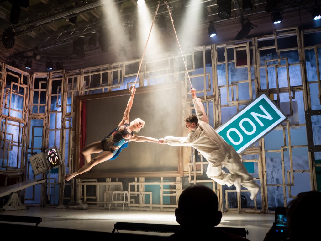 two aerialists swing around stage holding hands